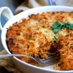 Spaghetti Pie with Three Cheeses in round white baking dish on blue striped towel with a wedge cut from it.