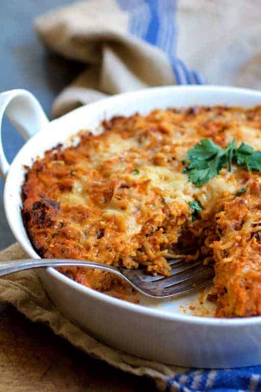 Spaghetti Pie with Three Cheeses in round white baking dish on blue striped towel with a wedge cut from it.