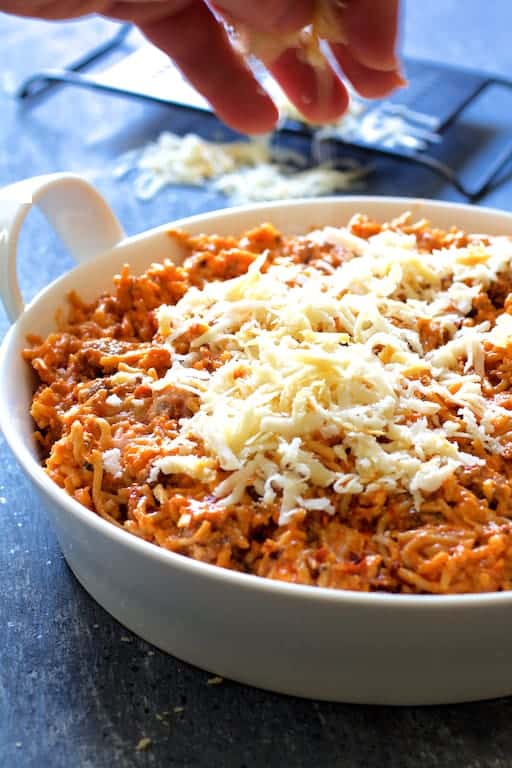 Photo of cheese being sprinkled over Spaghetti Pie with Three Cheeses.
