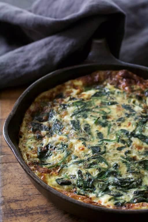 Photo of Spinach Leek and Feta Cheese Frittata in cast iron skillet with gray towel over handle.