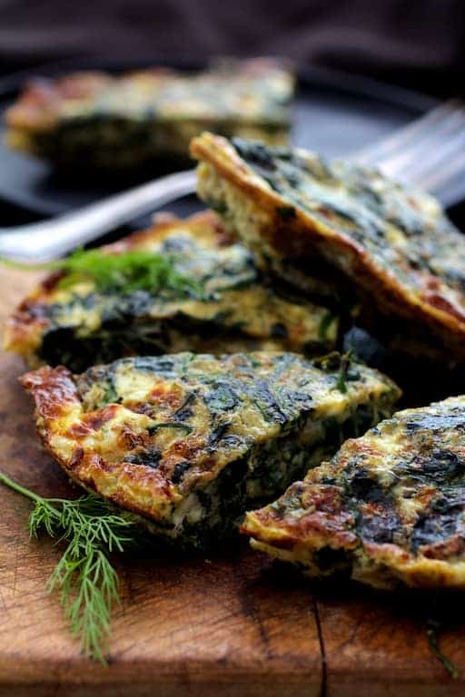 Close-up photo of frittata wedges on wood cutting board garnished with fresh dill.