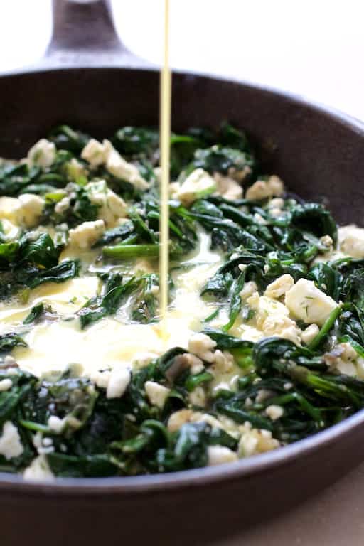 Photo of egg mixture being poured over spinach and leek combination in cast iron skillet.