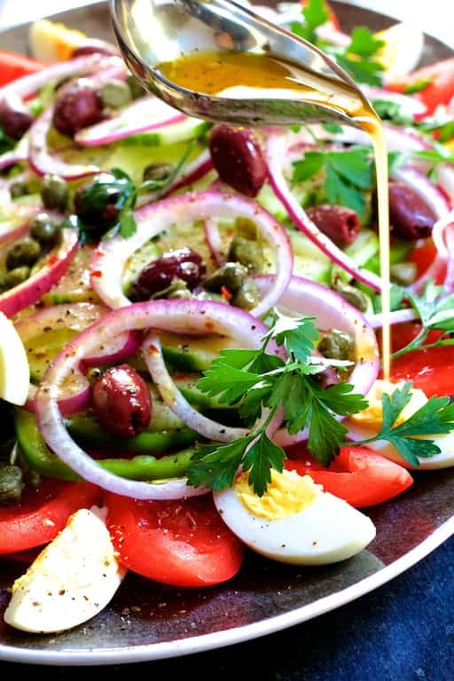 Photo of dressing being drizzled over salad from silver serving spoon.