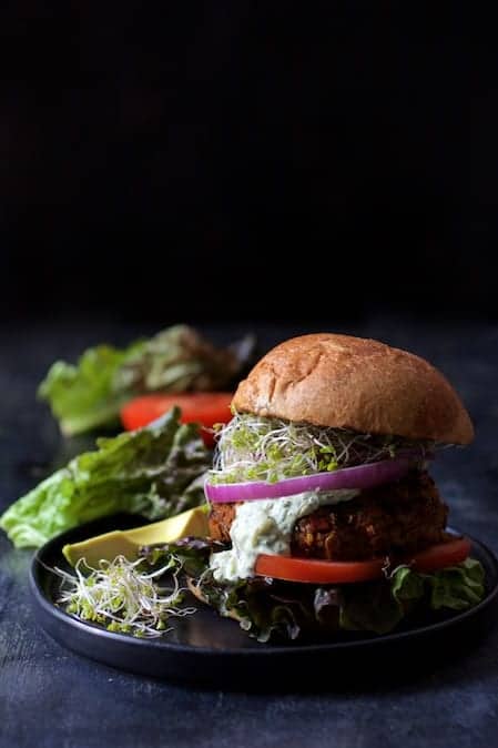 Photo of Lentil Walnut Veggie Burgers with Avocado Tzatziki Sauce on black plate.