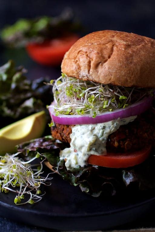 Close-up photo of Lentil Walnut Veggie Burgers with Avocado Tzatziki with tzatziki dripping down side of burger.