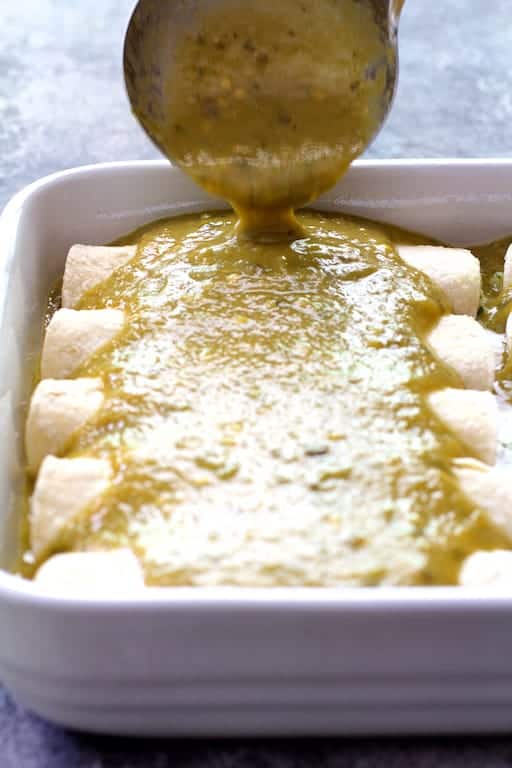 Photo of green chile sauce being poured over enchiladas.