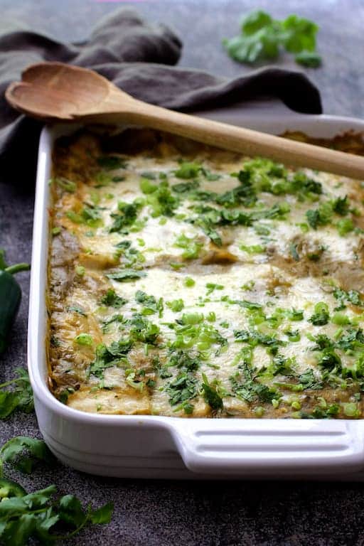 Photo of Lima Bean and Potato Enchiladas with Hatch Green Chile Sauce in white baking dish with wood serving spoon.