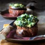 Beef Tenderloin Fillets with Spinach Cambozola Stuffed Mushrooms and Red Wine Sauce with steak knife on plate set on wood cutting board.