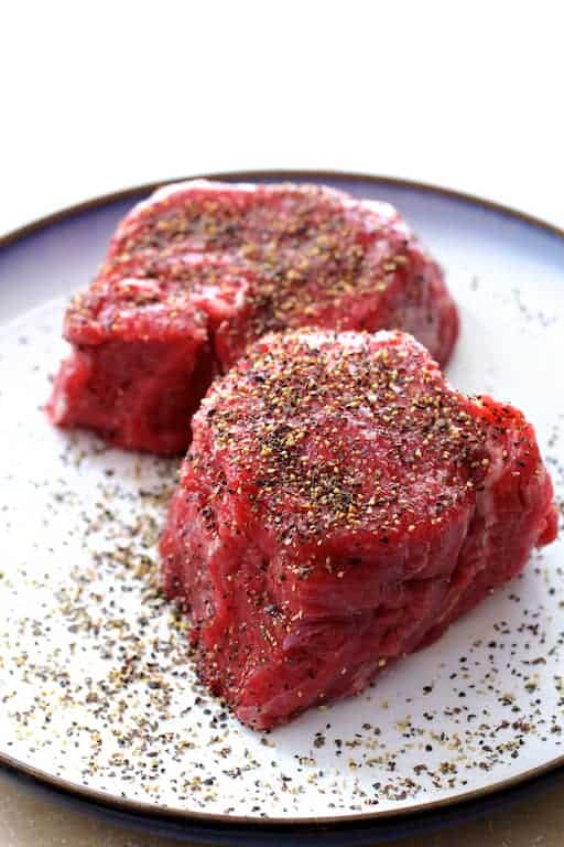 Photo of two raw uncooked beef fillets on plate.