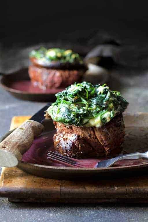 Beef Tenderloin Fillets with Spinach Cambozola Stuffed Mushrooms and Red Wine Sauce with steak knife on plate set on wood cutting board.