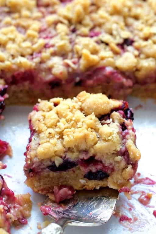 Close-up photo of a Blueberry Crumble Bar on silver pie server about to be removed from white baking dish.