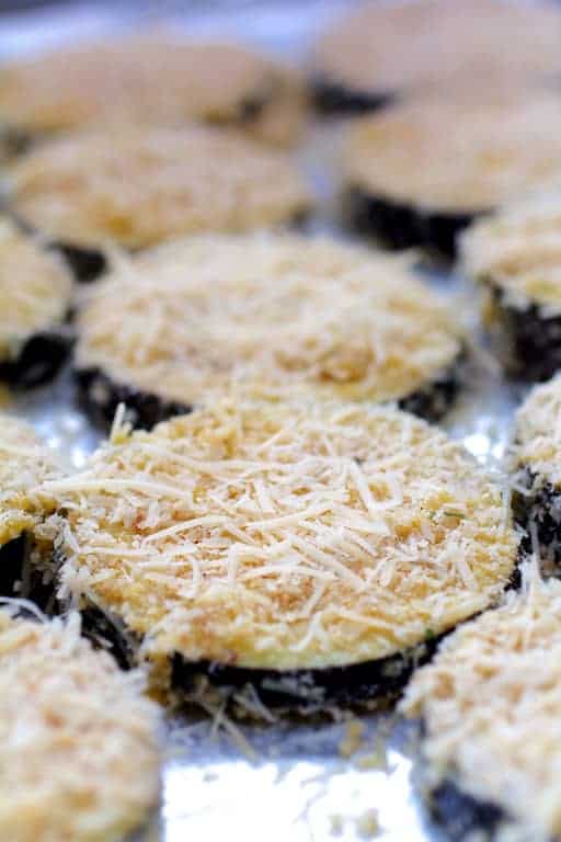 Photo of eggplant slices coated with breading and parmesan cheese on baking sheet before being baked..