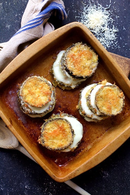 Top down photo of eggplant stacks with melty cheese between the layers in clay baking dish.