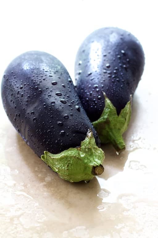 Photo of two whole freshly washed eggplants on marble surface.