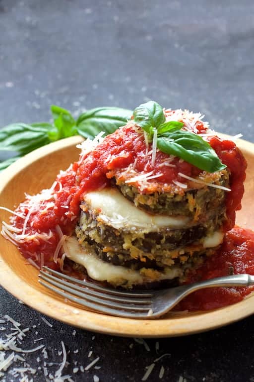 Close-up photo of an Eggplant Parmesan Stack in wooden bowl garnished with fresh basil and fork ready to eat.