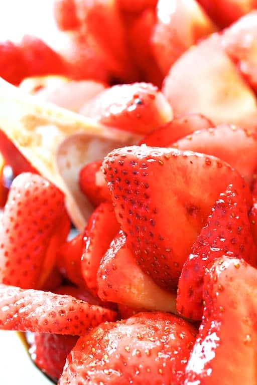 Close-up photo of strawberries being stirred with white spoon.