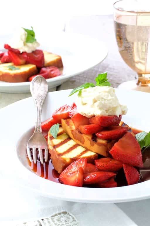 Photo of Grilled Pound Cake with Balsamic Macerated Strawberries and Mascarpone Cream on white plate with water glass in the background.