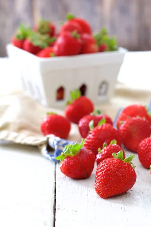 Photo of fresh berries on white painted wood surface with basket of berries in background.