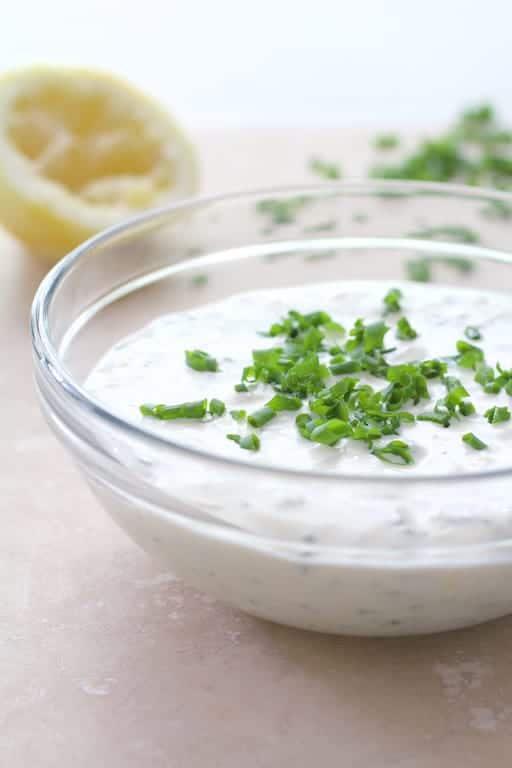 Photo of lemon chive aioli in glass mixing bowl garnished with chives.