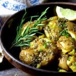 Rosemary Garlic Crushed Potatoes in brown ceramic dish garnished with fresh rosemary.