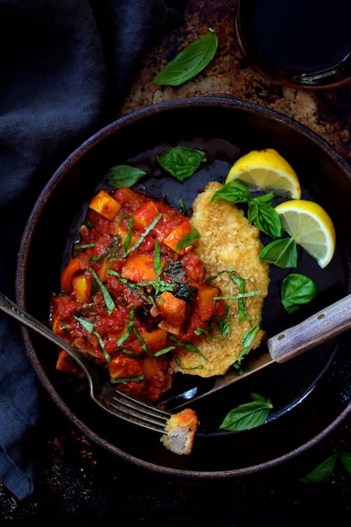Photo of Chicken Scallopini with Roasted Vegetable Ratatouille in clay dish garnished with fresh basil and lemon wedges.