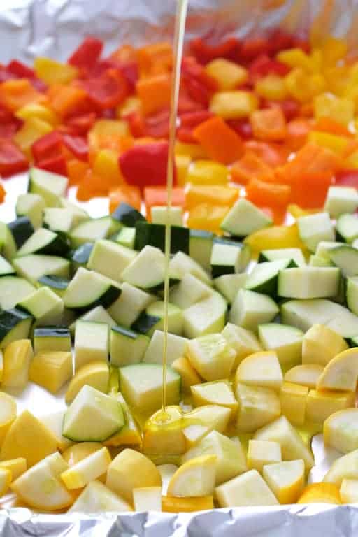 Photo of vegetables for ratatouille on baking sheet being drizzled with olive oil.
