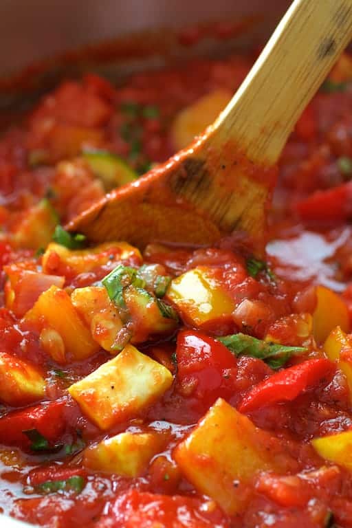 Close-up photo of vegetables being stirred in sauce with wooden spoon.