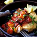 Chicken Scallopini with Roasted Vegetable Ratatouille in brown ceramic dish with knife and fork with a piece cut from the scallopini.