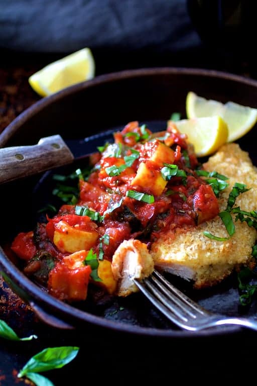 Chicken Scallopini with Roasted Vegetable Ratatouille in brown ceramic dish with knife and fork with a piece cut from the scallopini.