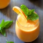 Chilled Cantaloupe Soup in a glass garnished with an orange wedge and fresh basil.