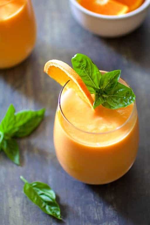 Chilled Cantaloupe Soup in glasses garnished with orange slices and fresh basil leaves.