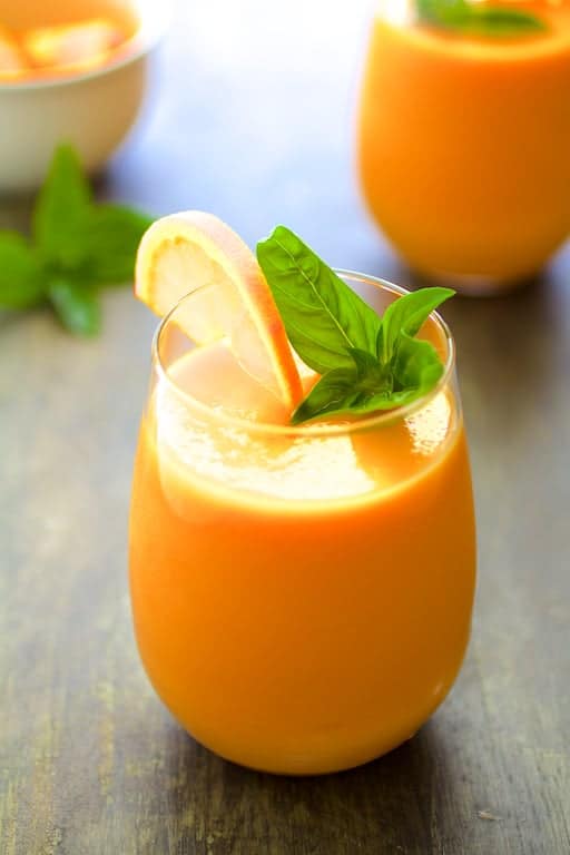 Chilled Cantaloupe Soup garnished with an orange wedge and fresh basil.