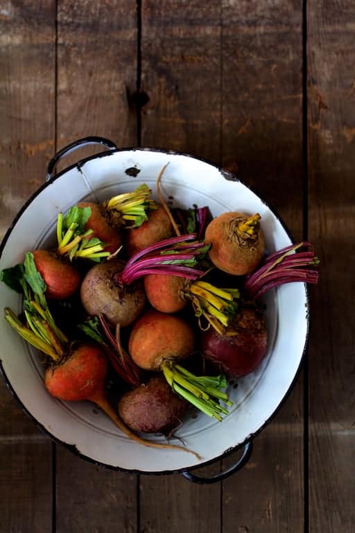 Photo of whole raw beets in antique white colander on wooden background.
