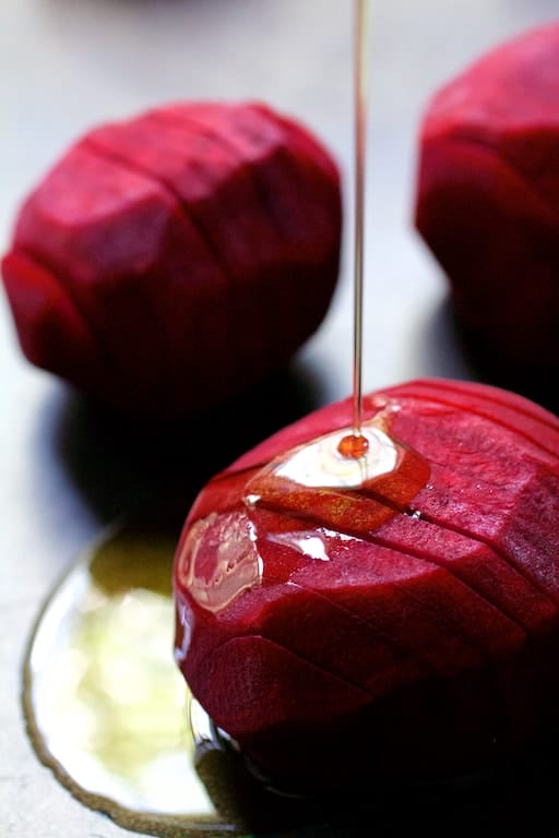 Photo of raw hasselbacked beets being drizzled with olive oil.