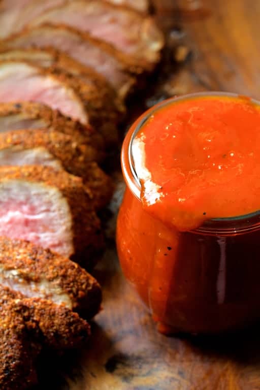 Close-up photo of sauce in glass jar with sliced pork tenderloin off to the side.