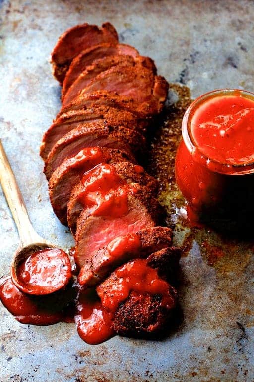 Spice Rubbed Pork Tenderloin with Peach Chipotle Barbecue Sauce on baking sheet with the sauce in a jar and spooned over the pork tenderloin.