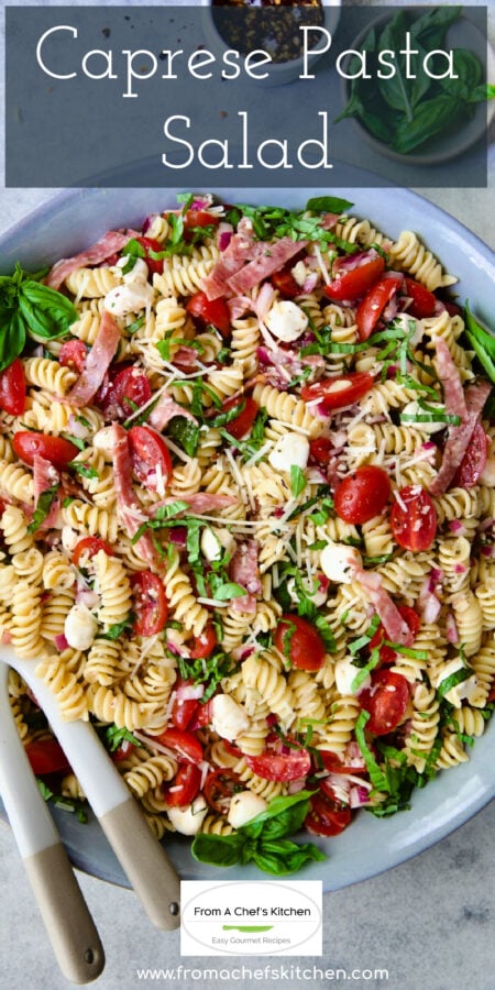 Pinterest graphic for Caprese Pasta Salad showing it in a in blue bowl being stirred with serving utensils.