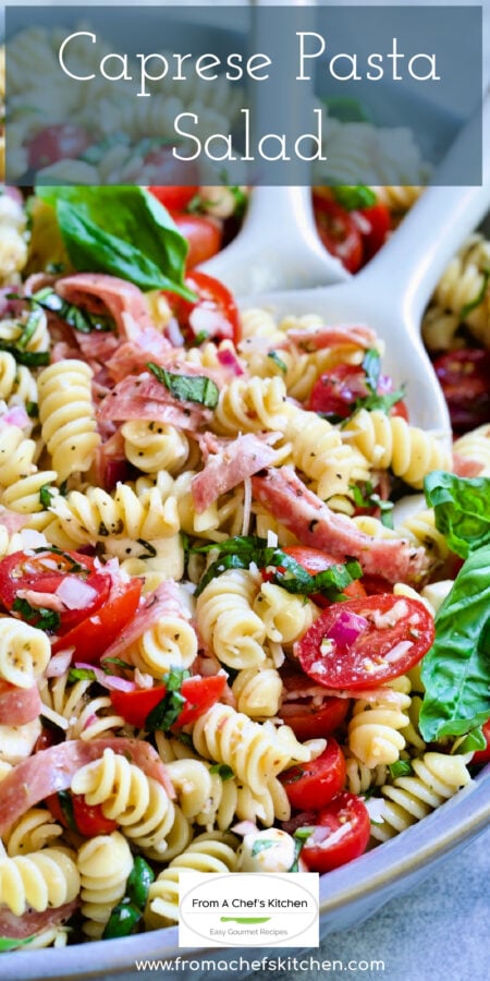 Pinterest graphic for Caprese Pasta Salad showing it in a in blue bowl being stirred with serving utensils.