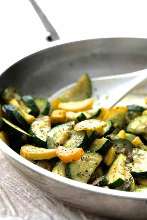 Close-up photo of zucchini and yellow squash being sauteed in stainless steel pan.