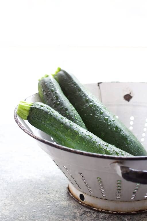 Photo of three freshly washed zucchini in antique white colander.