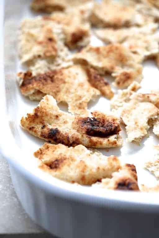 Process photo of first layer of naan pieces in white baking dish.