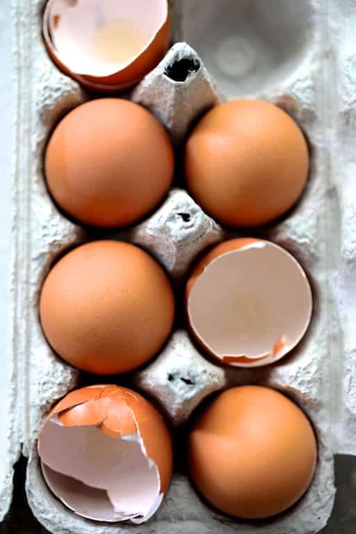 Photo of seven eggs in egg carton with four whole and three empty shells.