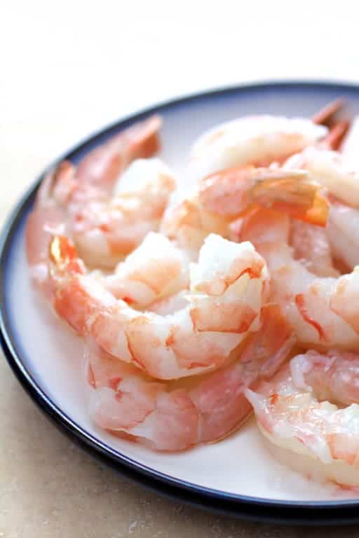 Photo of fresh, uncooked shrimp on white plate with blue rim.