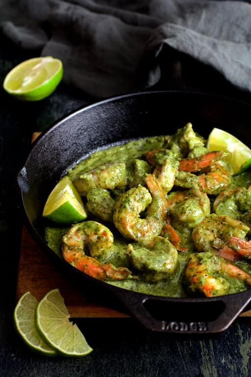 Photo of Shrimp in Avocado Butter in cast iron skillet garnished with lime wedges on wood trivet.