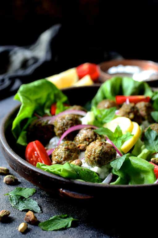 Photo of Turkish Turkey Meatball Lettuce Wraps with Tzatziki in clay dish with all the garnishes: Tomatoes, onion slices, lemon wedges, pistachios, mint leaves.