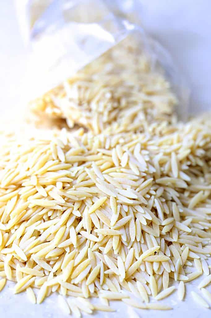 Photo of orzo being spilled out of bag onto surface.