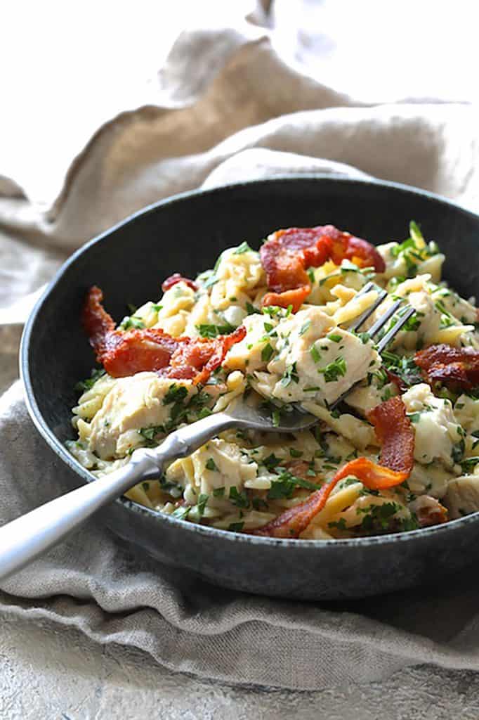 Photo of one serving of Creamy One Pot Chicken and Orzo Risotto with Bacon in black bowl.