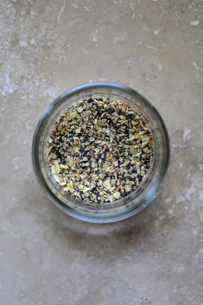 Photo of everything bagel spice in glass jar on gray surface.