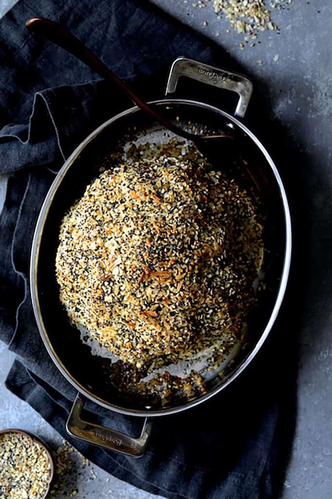 Photo of Everything Bagel Spice Whole Roasted Cauliflower in roasting pan on dark gray towel.
