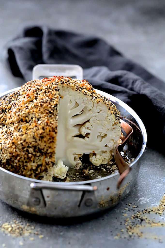 Photo of Everything Bagel Spice Whole Roasted Cauliflower in roasting pan with a wedge removed to expose the interior.